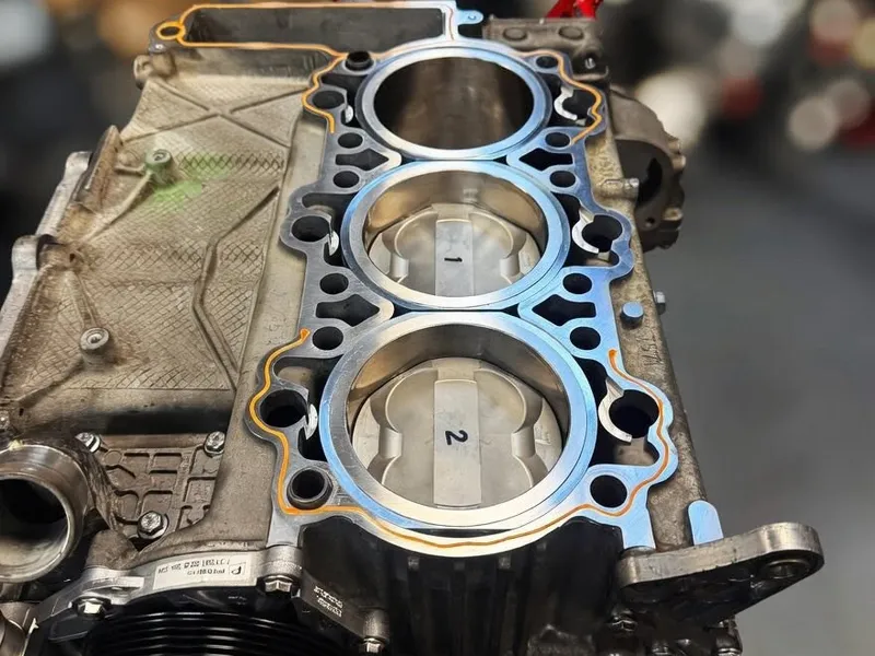 Crankcase half on an engine stand with a new head gasket laid on, the workshop lights out of focus behind.