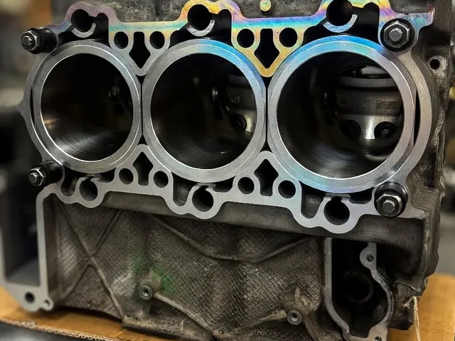 Crankcase half with three new liners and a head gasket in place, on the bench in the engine room with the workshop out of focus behind.