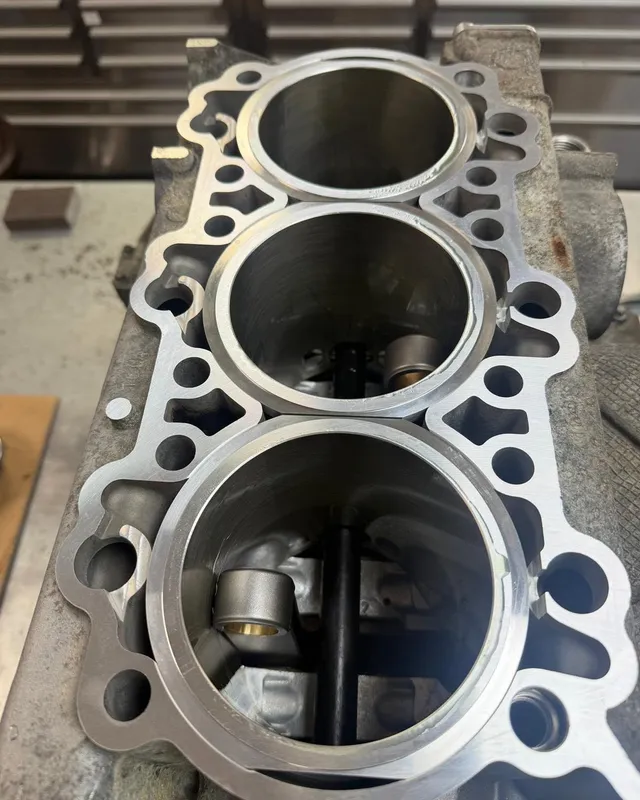 Looking straight down three cylinder bores in a crankcase half, with the crankshaft visible at the bottom.