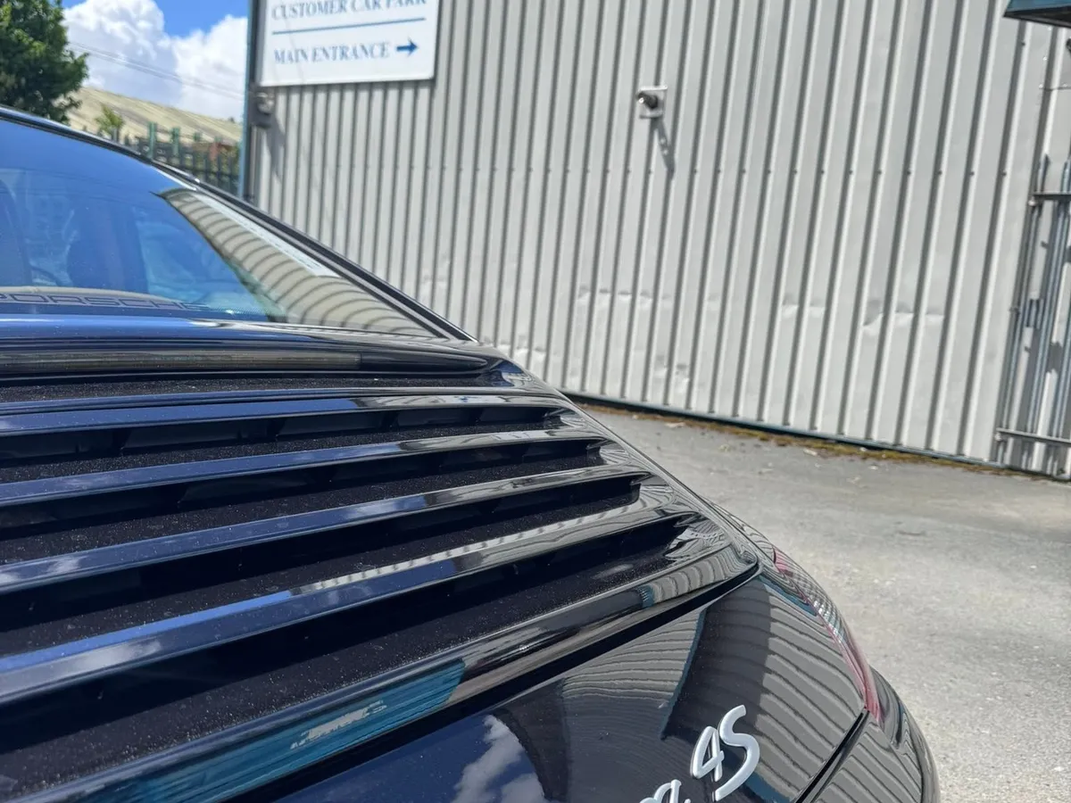 The rear of a black 997 Carrera 4S in the yard, with the Hartech sign and the entrance signs on the building behind.