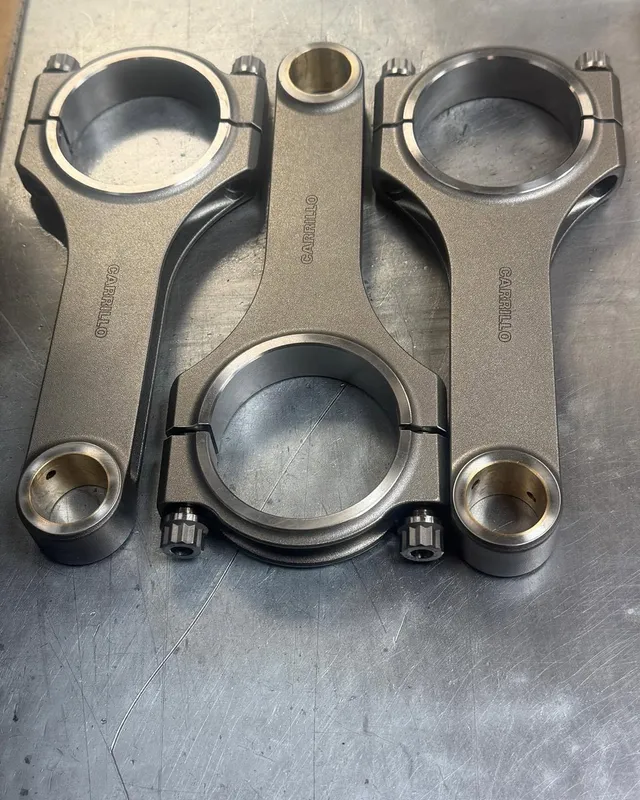 A single forged H-beam connecting rod lying on the bench.