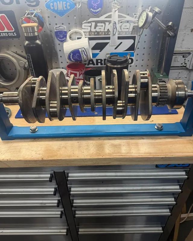 A crankshaft on a blue stand on the engine room bench with its bearing shells laid out beside it.
