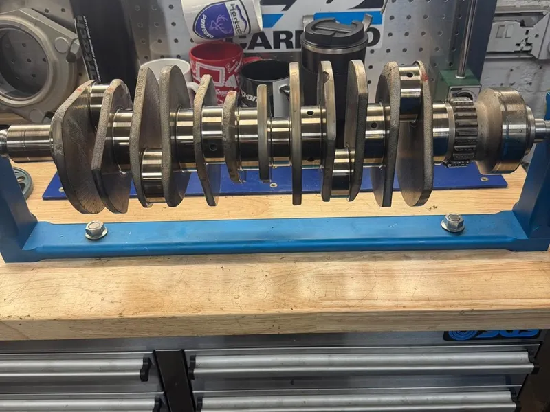 A crankshaft on a blue stand on the engine room bench with its bearing shells laid out beside it.