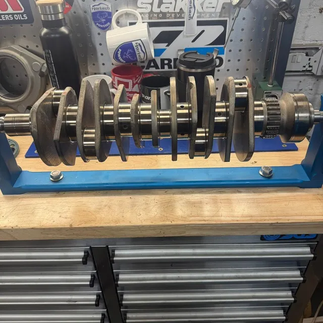 A crankshaft on a blue stand on the engine room bench with its bearing shells laid out beside it.