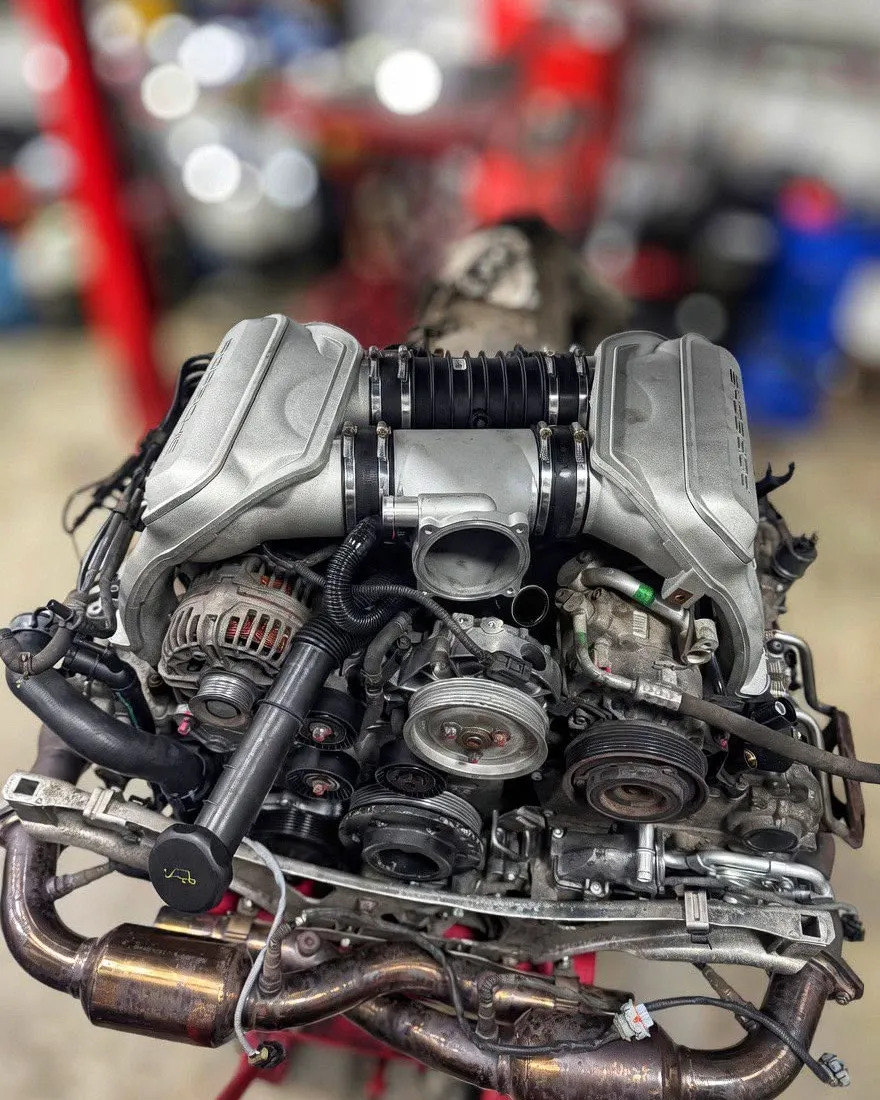 A complete M96 engine with intake manifold, alternator and exhaust headers, on a red engine stand in the workshop.