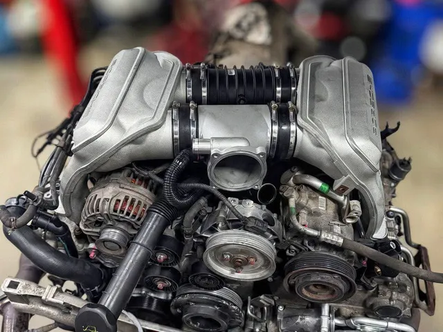 A complete M96 engine with intake manifold, alternator and exhaust headers, on a red engine stand in the workshop.