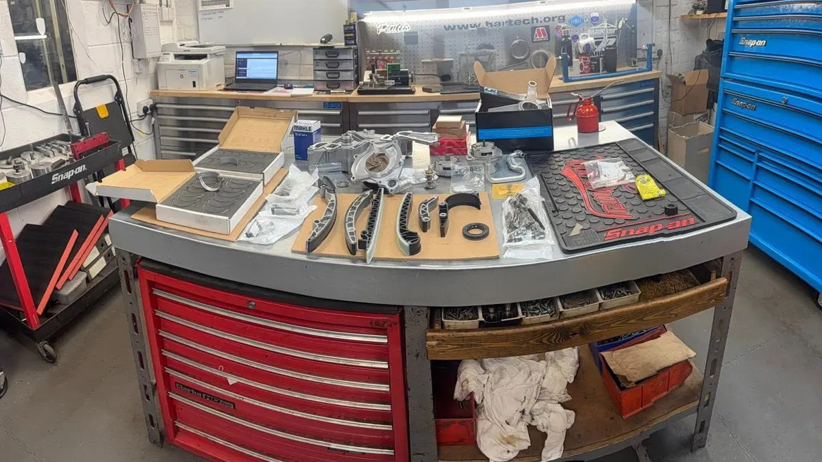 The engine room bench with a strip-down laid out on a mat: timing chains, sprockets, bolts and gaskets, with tool chests behind.
