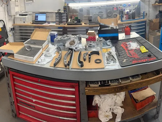 The engine room bench with a strip-down laid out on a mat: timing chains, sprockets, bolts and gaskets, with tool chests behind.