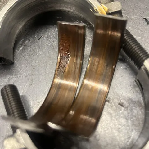 Two big-end bearing shells sitting in a rod cap, both discoloured and worn.