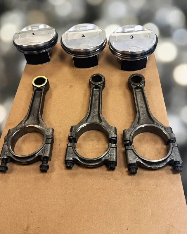 Three pistons and three connecting rods laid out on card on the bench.