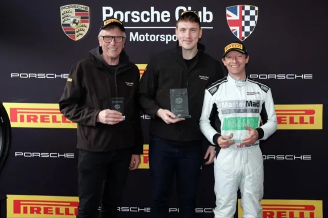 Three people on a Porsche Club Motorsport podium backdrop holding trophies.
