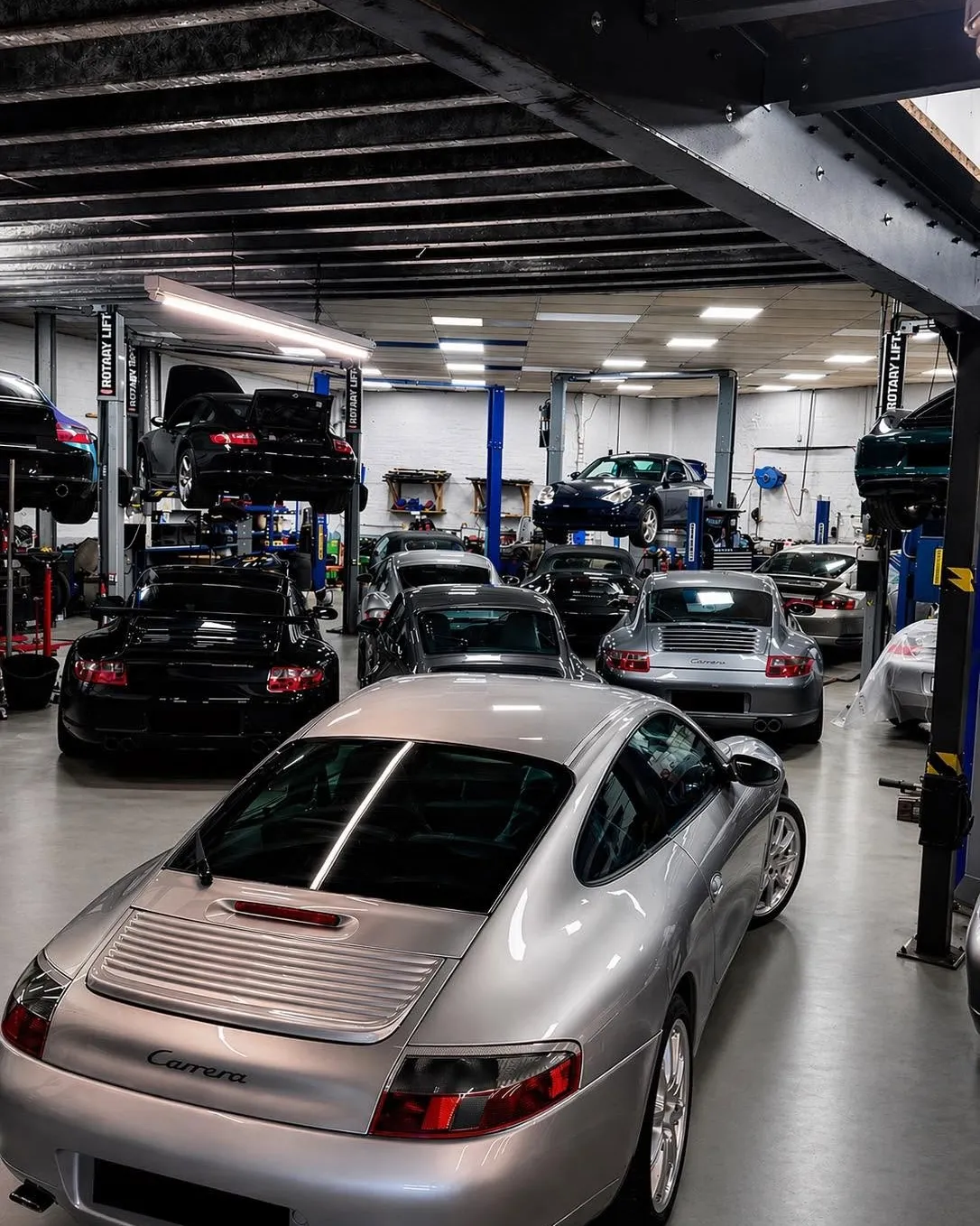 A silver 996 Turbo in the main workshop with cars on two-post lifts down both sides of the bay.