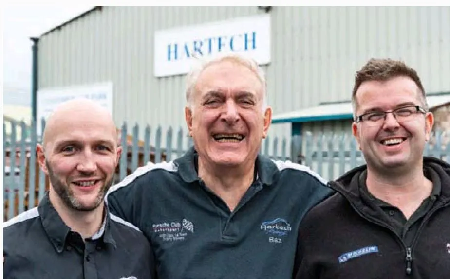 Three of the Hartech team outside the workshop beneath the Hartech sign, Baz Hart in the centre.